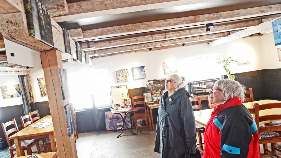 Nyfikna. Gun-Marie Kumbrandt och Carita Gustavsson bor inne i Örsundsbro samhälle och har tagit sig en promenad genom snömodden för att ta sig en kopp kaffe och en godbit. De stannar upp och förundras över verken som hänger från takbjälkarna.