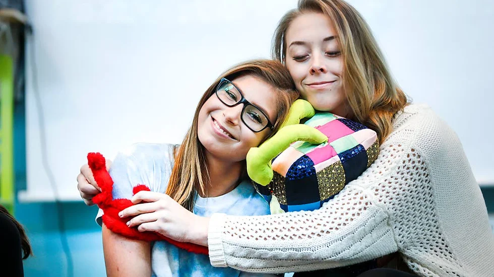GENUS. Tygfiguren Genus får en kram av Amelia Kämpeberg och Julia Grönberg.