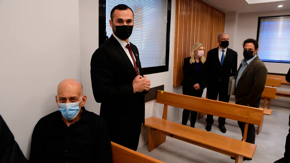 Ehud Olmert, till vänster i bild, fälls för att ha förtalat Benjamin Netanyahu och hans fru, som står i bakgrunden.