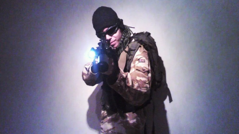 22-åringen poserar i militäruniform och med vapen.