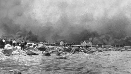 3 juli 1908. Vid branden klarade sig sågverket, skolan och bygmästarbostaen. Men det som varit mellan 500 och upp till 1.200 människors hem under 37 år blev lågornas rov. I bildens vänsterkant ser man öns invånare följa den dramatiska eldsvådan.