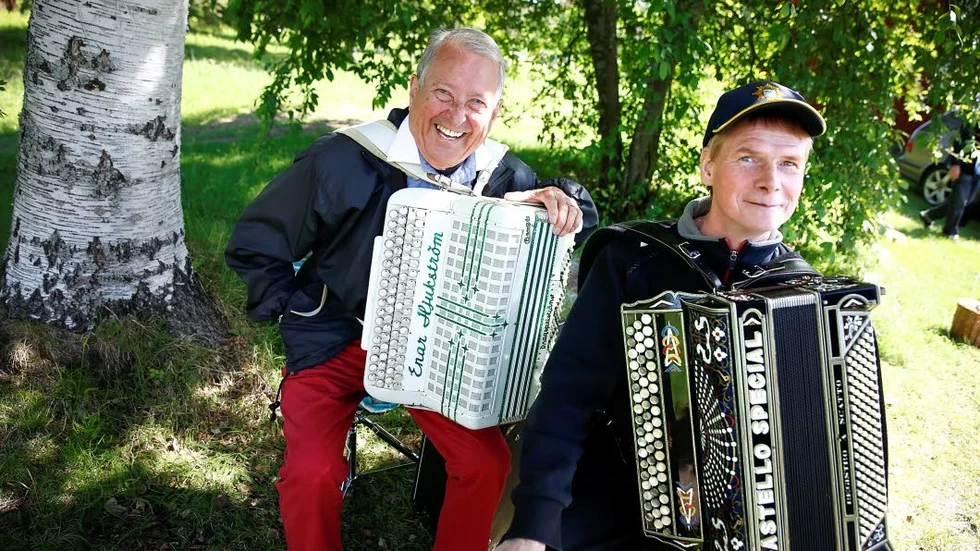 Glada dragspelare. Enar Hjukström, Piteå och Per Stenelund, Avan, laddar upp i skuggan under en stor björk innan de ska upp på scenen och spela.