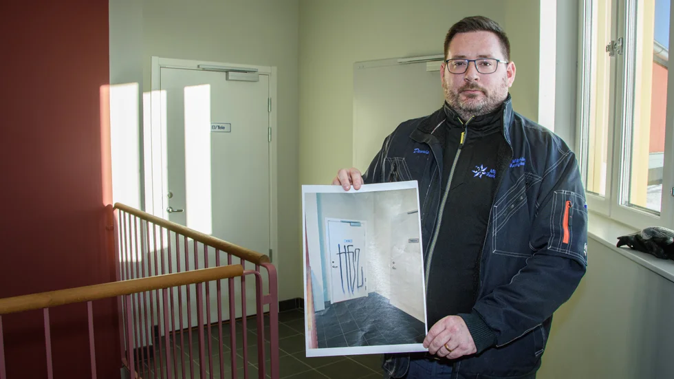 Dennis Wikstén visar upp hur klottret såg ut för en tid sedan på dörren bakom honom. Han polisanmälde och informationen kom även med i den lägesrapport som kommunen delger och som sedan kan diskuteras på trygghetsfrukosten.