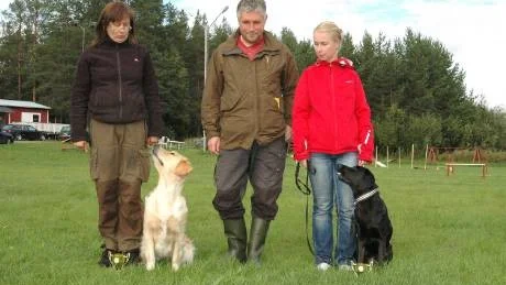PÅ PRISPALLEN. Domare Peter Andersson mellan de två förstapristagarna under helgens lydnadsklasstävling  på Kalix Brukshundklubb. Carola Berg med sin golden retriver Cassmick ring of roses fick flest poäng i lydnadsklass ett och Britt-Louise Åberg med blandrasen Hilda hamnade högst med sina 188p i lydnadsklass två.