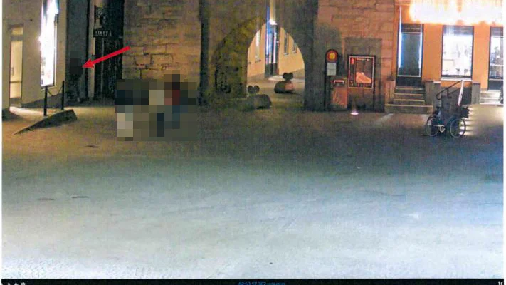 Gärningsmannen är utmarkerad med en röd pil där han väntar på offret. Övriga personer på bilden har inte något med utredningen att göra.