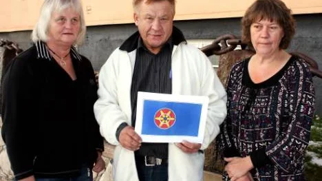 Birgitta Pounu, Björnar Seppola och Gertrud Monlund visar upp flaggan som Kvenlandsförbundets medlemmar har röstat fram.