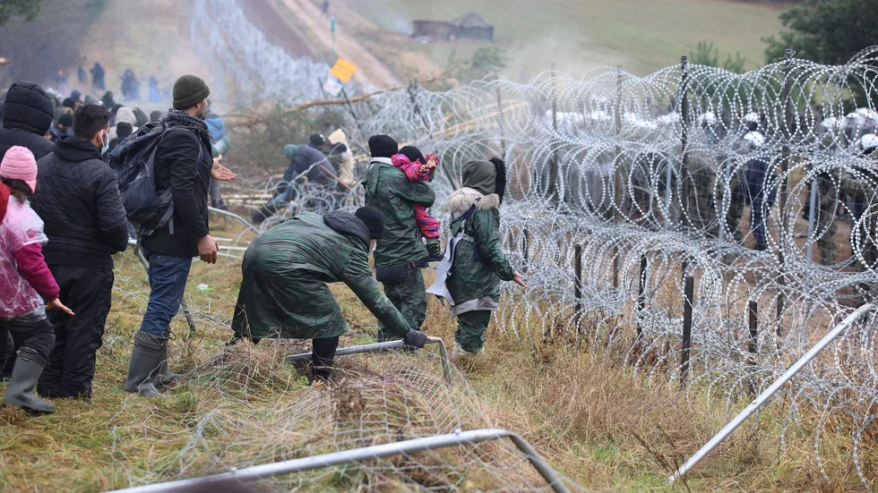 Migranter med barn vid gränsen Belarus–Polen. På andra sidan syns de polska soldaternas vita hjälmar.