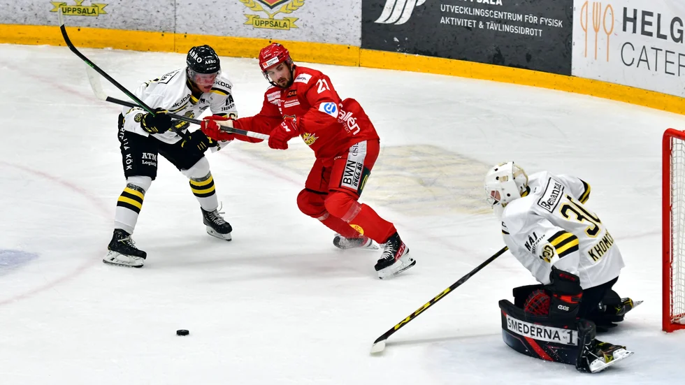 Johan Eriksson i en puckduell med en AIL-back och målvakten under onsdagens match i Upplands Bilforum Arena.