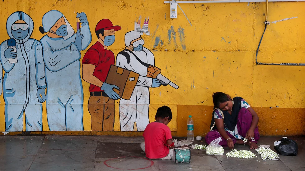 En kvinna sitter med sin son intill en muralmålning föreställande samhällsviktiga arbetare i kampen mot covid-19 i Bombay (Mumbai).
