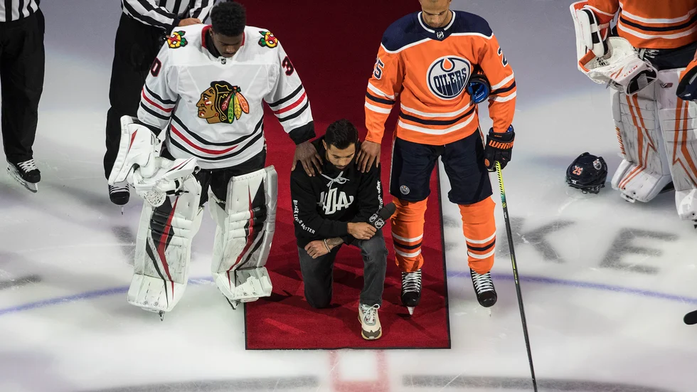 Minnesotas Matt Dumba står på ett knä under USA:s nationalsång, flankerad av Chicagos Malcolm Subban och Edmontons Darnell Nurse, när NHL inledde playoffserien med att markera mot rasism.
