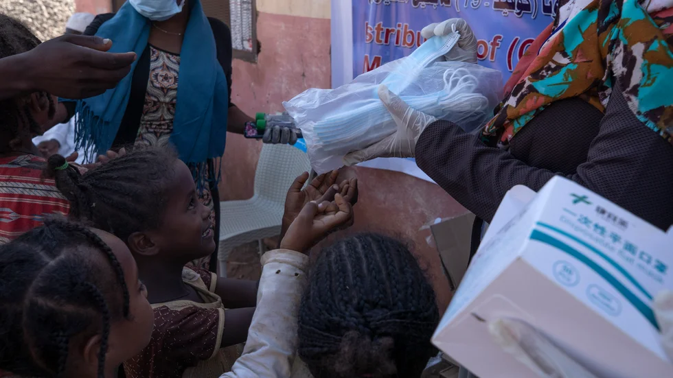 Hjälparbetare delar ut munskydd till barn som flytt från Tigray till ett flyktingläger i östra Sudan.