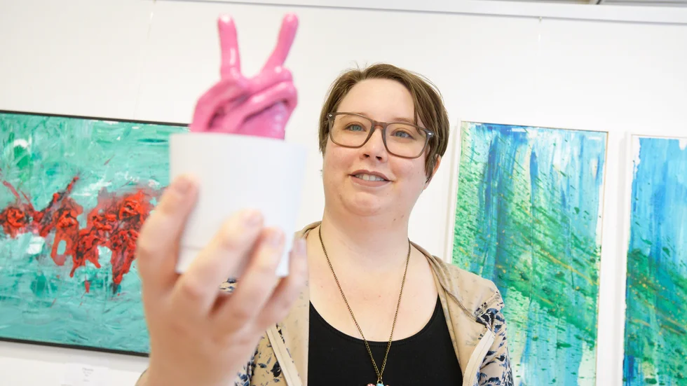 Malin Lundberg skapar i många olika tekniker, bland annat lera. Här håller hon i en hand som formar ett fredstecken i rosa. 