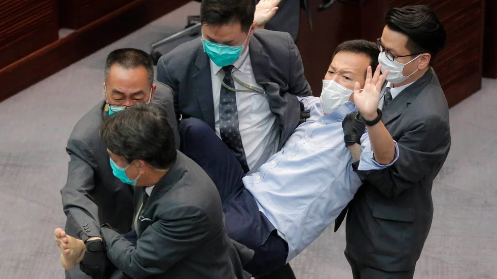 Den prodemokratiske dåvarande ledamoten i Hongkongs lagstiftande församling (Legco) Ray Chan bärs bort av säkerhetsvakter efter en protest i kammaren. Bild från i maj.