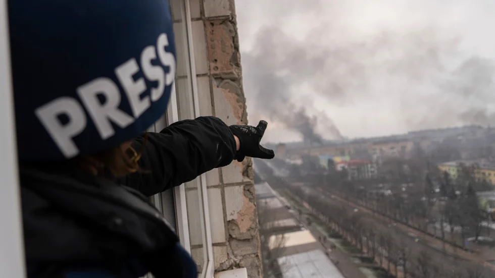 Nyhetsbyrån AP:s fotograf Jevhen Maloletka pekar mot röken som stiger efter attacken mot ett sjukhus för mödravård i den belägrade ukrainska staden den 9 mars.