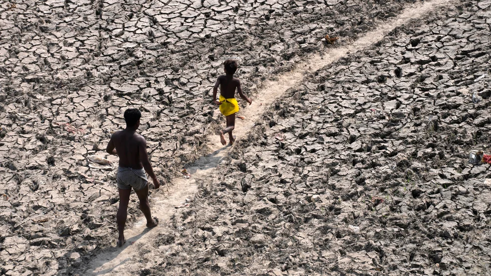 En man och en pojke går längs en nästan uttorkad flodbädd i Delhi i Indien.
