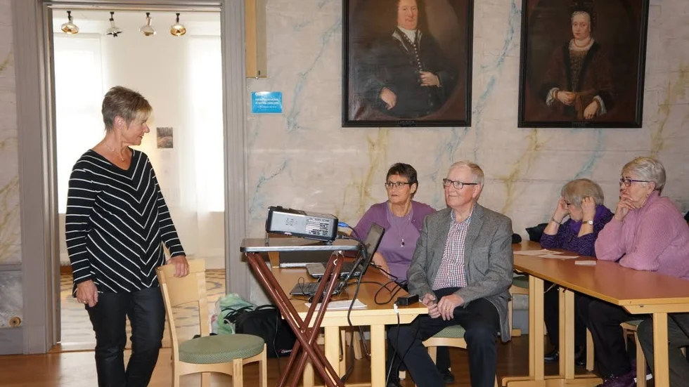 Berättelse. Lisbeth Lindmark välkomnar föredragshållarna, Barbro och Ivar Gustafsson. På väggen bakom syns porträtt av Daniel Solanders far och mor.