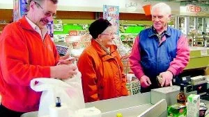 Helge Karlsson, en gammal bekant till Tyra Ossiansson, passar på att få en pratstund medan Börje Lundén servar kunden med nedpackningen av varorna.