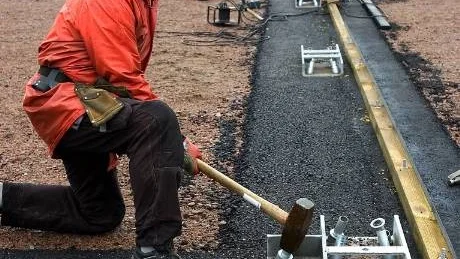 Nu är byggandet av Krokeks nya inomhushall igång igen, efter nästan tre månaders stiljtje. På bilden slår Ulf Eklund, närmast, och Morgan Broberg ner så kallade jordankare, där man förankrar hallen i asfaltsbården. Foto: Anita Kjellberg