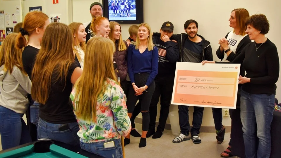 Anne Bergman Gustavsson lämnar över en check på 20 000 kronor till personal och ungdomar på plats vid fritidsgården i Kisa. Foto: Morgan Karlsson