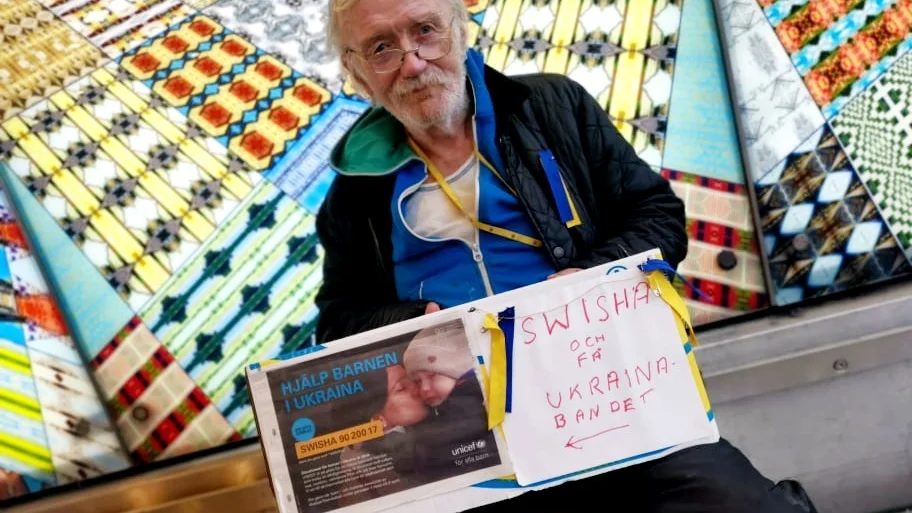 Kaj Furälv sitter nere vid centralstationen och ger bort sina egentillverkade Ukraina-band i utbyte mot att man swishar en summa till UNICEF.