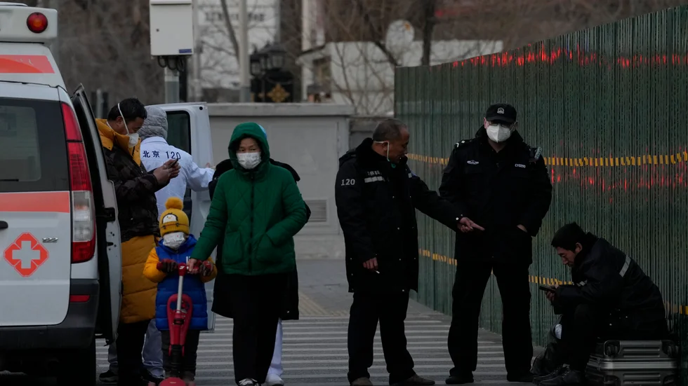 Kinesisk polis kontrollerar en man som vilar på sitt bagage i Peking under fredagen.