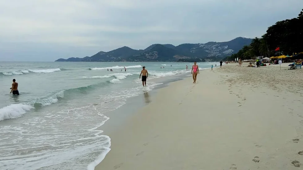 Turister går på stranden på Koh Samui som tros drabbas av den tropiska stormen Pabuk under fredagen.