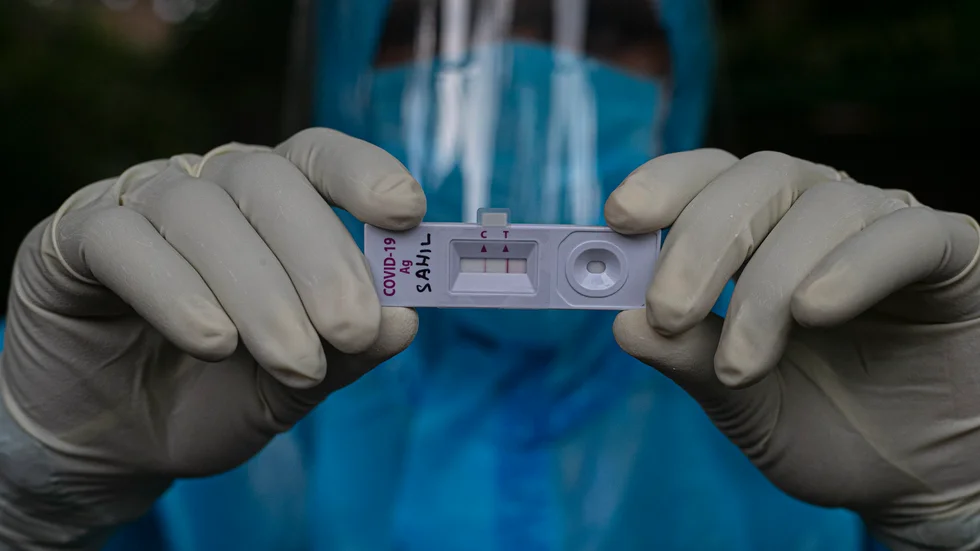 En vårdanställd i staden Gauhati i delstaten Assam i Indien håller upp ett positivt covid-19-test. Bilden är från i lördags.