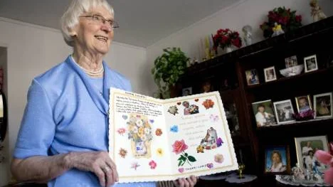 Nina Nyström med bilder på nära och kära i bokhyllan och ett jättestort födelsedagskort från bästa väninnan i Polen i hand. Hon fyllde 80 år den 24 april.FOTO: Pär Bäckström
