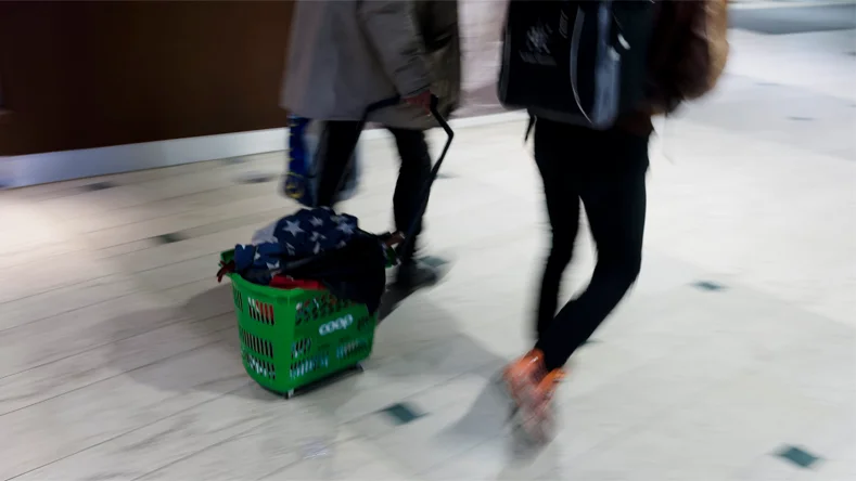Två personer går med en rullkorg från en matbutik. Genrebild.
