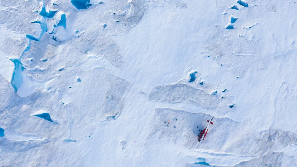 Forskare runt en helikopter, nere till höger i bild, på den grönländska Helheim-glaciären. Fotot togs 2019, då instrument sattes upp på glaciären för att mäta hur snabbt den smälter.