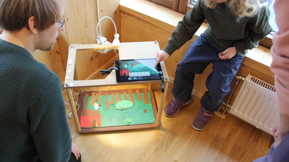 Illustratör Kalle Landegren hjälper Walter Tröen att spela in sin stop-motion-film i studion som består av en liten möbel med en ipad som fotar pappret och figurerna nedanför.