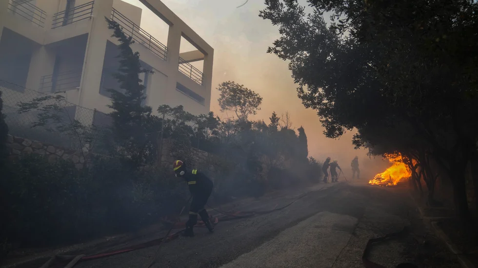 Brandmän försöker släcka i närheten av ett hus i Penteli-bergen.