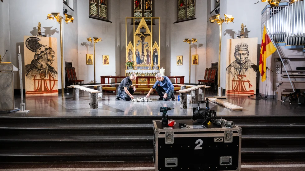 Kyrkvaktmästarna Carl-Sören Edfast och Jan Hellström gör i ordning eldstad längst fram i domkyrkan med träbänkar omkring. Här ska ärkebiskopen ta plats och några möta samiska representanter som kommer att berätta om de oförrätter som skett. Sedan ska ärkebiskopen falla på knä och be det samiska folket om ursäkt. På vardera sida står den samiska konstnären Anders Sunnas bilder med stora porträtt av samer.