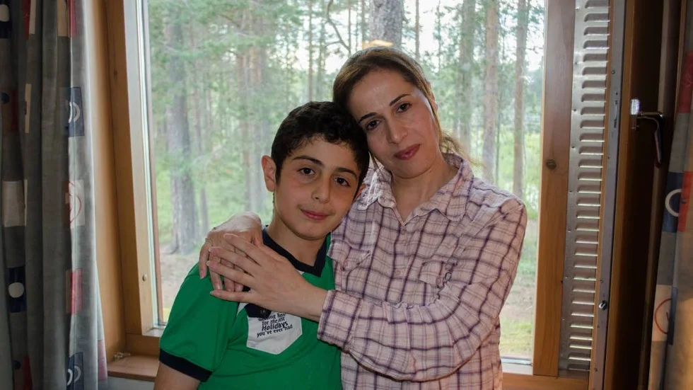 Mor och son. Rayan, 12 år, och mamma Shefa Abodaka framför sitt fönster på rummet i hotell Nordkallotten. Hemma i Syrien kunde de aldrig visa sig i fönstret utan att riskera att bli skjutna, berättar Rayan.