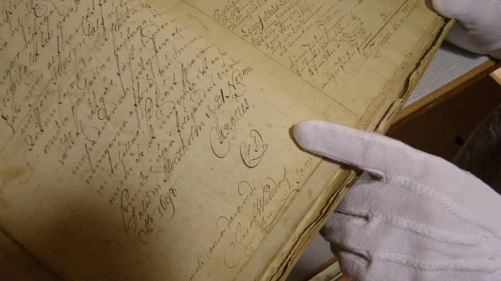 Denna bok från 1600-talet med Karl XII:s namnteckning "Carolus" finns bland Landsarkivet i Vadstenas vårdrelaterade arkivhandlingar. Händerna tillhör arkivarie Anna Eklundh-Jonsson.