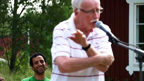 Poeten Sven Nyberg står vid mikrofonen under helgens tävling på Kulturgården. Hans humoristiska framträdande inkluderade hela kroppen, vilket tycktes roa medtävlanden Samed Salman som sitter i bakgrunden och väntar på sin tur.