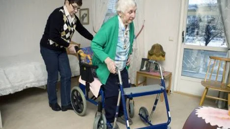Sigrid tar rullatorn från rullstolen till fåtöljen.