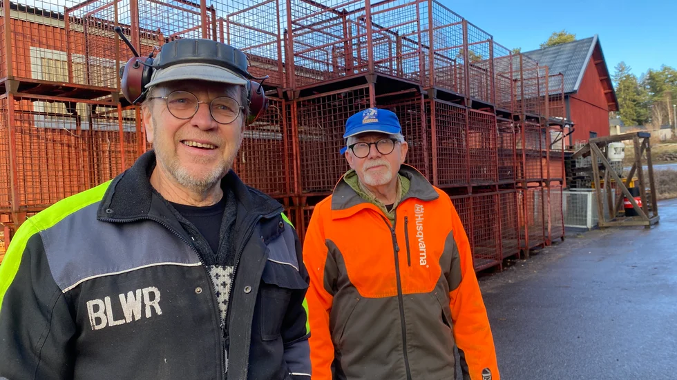 Karl-Gunnar Karlberg och Bengt Fredriksson framför de tomma vedburarna på Västerviks vedfabrik. All torr ved är slutsåld och de jobbar nu med att fylla burarna igen, med ved till nästa höst.