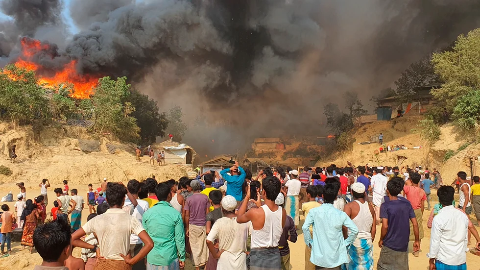 Människor ur folkgruppen rohingya framför röken och lågorna efter branden som blossat upp i flyktinglägret Balukhali i södra Bangladesh.