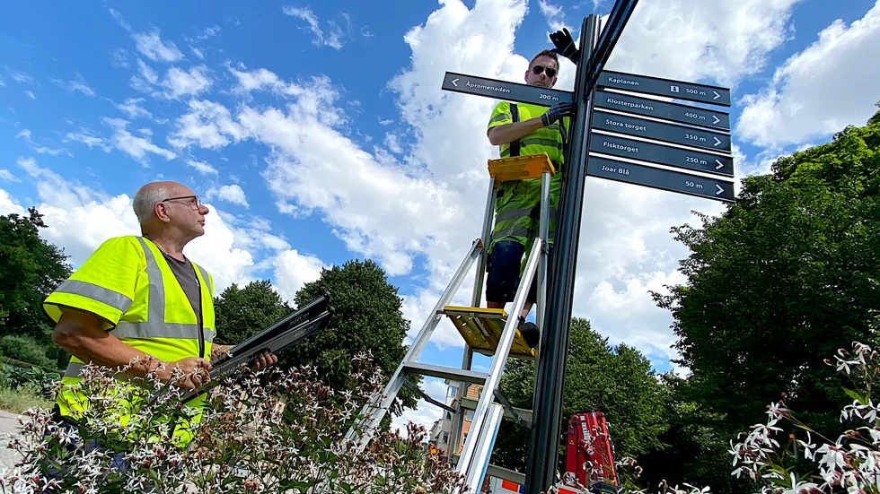Nya hänvisningsskyltar sätts upp i centrala Enköping. Roine Andersson, parkenheten och Åke Lindén från gatuavdelningen, hjälps åt med monteringen av de sista skyltarna i Drömparken.