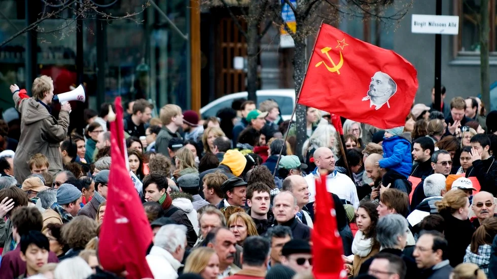 Hundraårig tradition (V) – fana med Sovjetsymbolen och diktatorn Lenin på 1 majmöte (V) i Stockholm 2010, med deltagande av kommunister från närstående utländska partier.