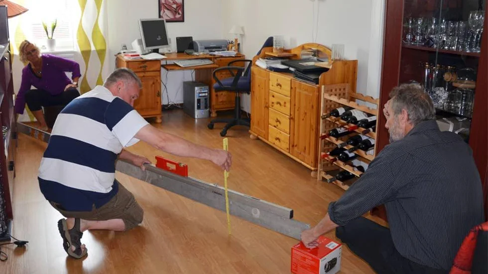Här visar Monica Lantto, Bosse Nilsson och Tommy Martinsson hur stor lutningen är på vardagsrumsgolvet. "Det lutar 16 cm."