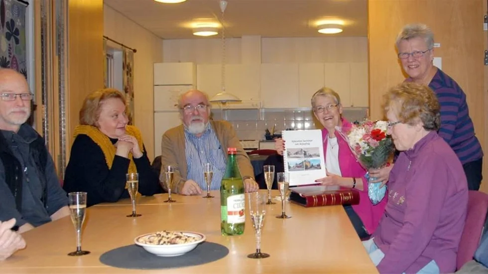 Elisabet Arvidson visar upp sitt senaste verk, ”Vykorten berättar om Arjeplog” för sina vänner i frimärksklubben. Fr.v. Roy Andersson, Mona Rönnholm, Stig Lundström, Elisabet med boken, Charlotte Nordgren, med blomsterkvasten och Margareta Häll.