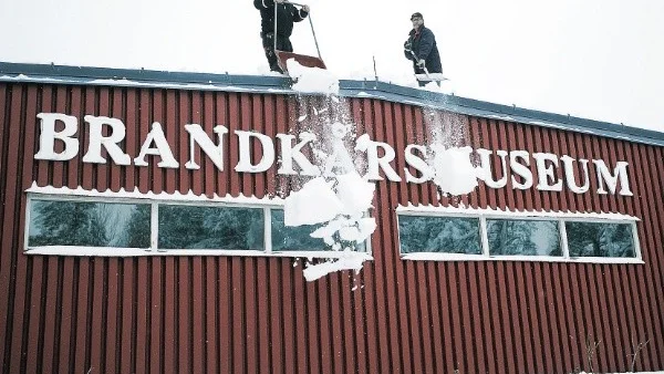 – Vi räknar med cirka 60 ton snö på museets tak, så det finns lite att skotta och skyffla ned, säger Mikael Strid, till vänster som här får hjälp av Bosse Svensson uppe på Brandkårsmuseets tak i Simonstorp.Foto: Janne Forsby