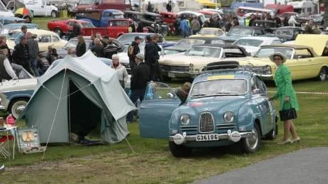 Sibylla Gustafsson poserar vid sin vinnande Saab i tidstypiska kläder från 1960-talet. Lägg märke till 60-talstältet och många andra veteranbilar i bakgrunden.