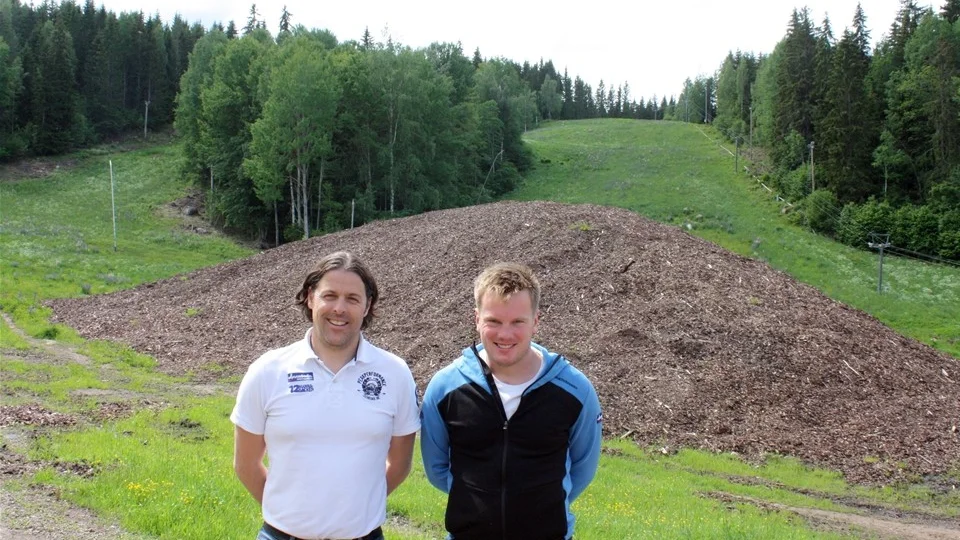 Tolvmannabackens vd Johan Larsson och driftansvarige Jonathan Bexell framför 15 000 kubikmeter sparad snö under ett tjockt lager flis och bark. Foto: Lars-Göran Bexell