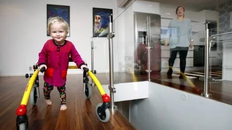 Noelle går inte som andra jämnåriga barn. En utvecklingsförsening - som delvis är knuten till hörselskadan - medför att hon ännu bara kan gå med stöd av en specialbyggd rollator.