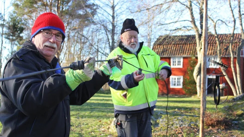 Lasse Vigertsson och Roland Thorstensson hänger upp de kulörta lamporna, som bidrar till att det blir juligt och mysigt i parken på lördag.