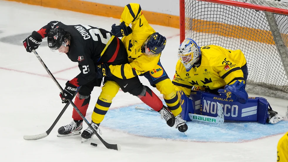 Sveriges målvakt Melker Thelin ser på medan backen Viggo Gustafsson kämpar mot Kanadas Easton Cowan i kampen om pucken.
