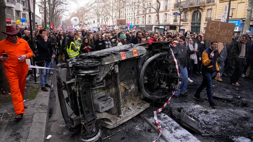 Demonstranter i Paris går förbi en bil som stuckits i brand under lördagens protester mot regeringens planer på att höja den franska pensionsåldern från 62 till 64 år.